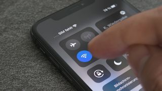 iPhone에서 Wi-Fi 핫스팟을 설정하는 방법에 대한 문서를 나타내는 제어 센터에서 Wi-Fi 버튼을 탭하는 손가락을 보여주는 iPhone 이미지