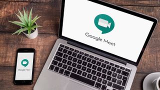 나무 탁자 위에 놓여 있는 노트북과 휴대전화에 표시되는 Google Meet 로고