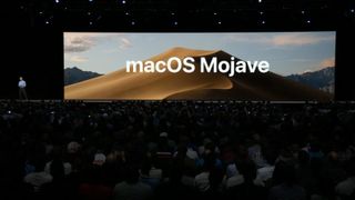 화면에 macOS Mojave 이미지가 표시된 상태로 컨퍼런스에서 발표하는 남자