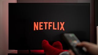 발을 앞에 두고 손을 잡고 리모컨을 들고 TV 화면에 표시되는 Netflix